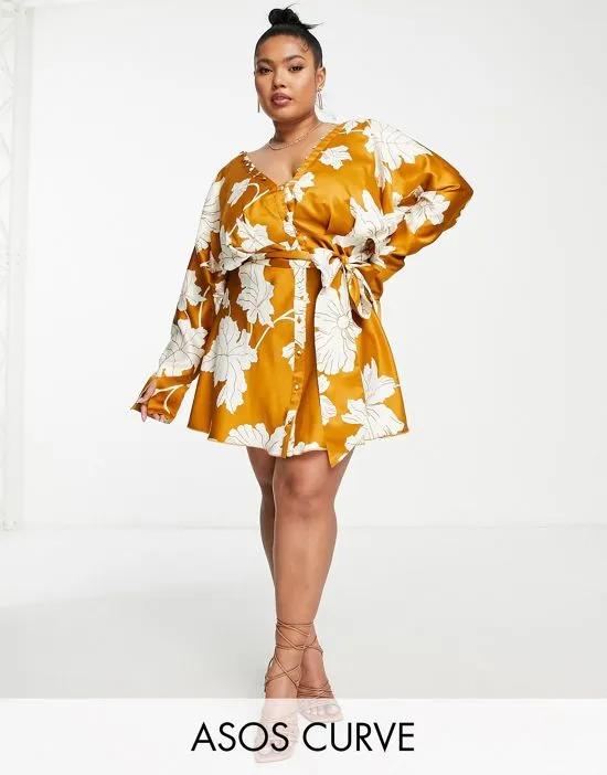 ASOS DESIGN Curve satin batwing mini dress with button front detail and tie front in mustard floral print